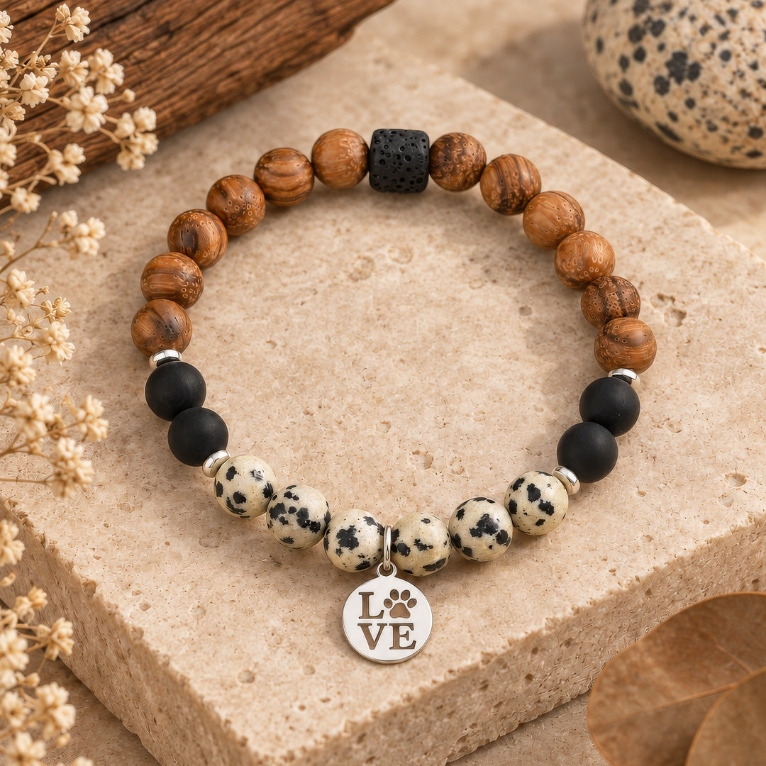 Handcrafted bracelet featuring 8mm dalmatian jasper and lava rock beads paired with warm wooden accents. Finished with delicate 4mm hematite silver rondelles and a stainless steel love dog paw charm in silver. Stretchy design fits most wrists comfortably. Perfect for gemstone lovers and dog enthusiasts alike.