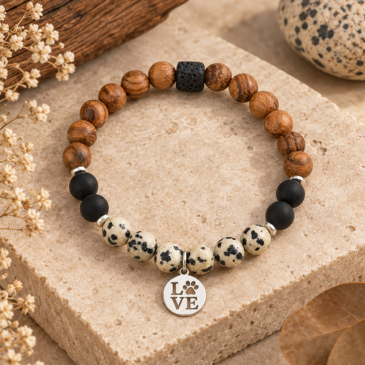 Handcrafted bracelet featuring 8mm dalmatian jasper and lava rock beads paired with warm wooden accents. Finished with delicate 4mm hematite silver rondelles and a stainless steel love dog paw charm in silver. Stretchy design fits most wrists comfortably. Perfect for gemstone lovers and dog enthusiasts alike.